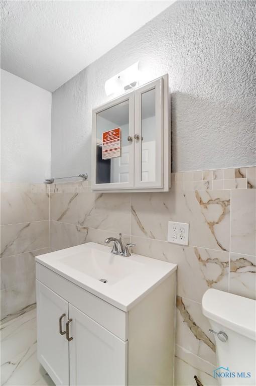 bathroom with vanity, toilet, and tile walls