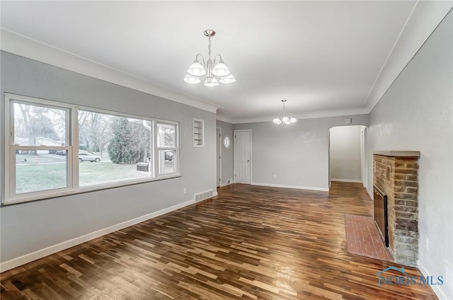 unfurnished living room with ornamental molding, a chandelier, dark hardwood / wood-style floors, and a brick fireplace