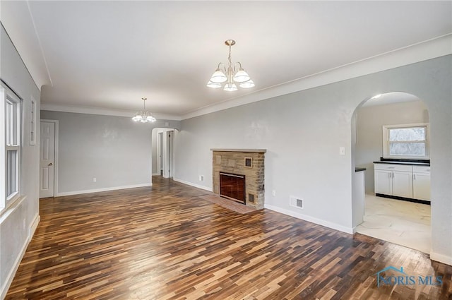 unfurnished living room featuring a fireplace, ornamental molding, dark hardwood / wood-style floors, and a notable chandelier