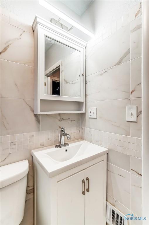 bathroom with vanity, toilet, and tile walls