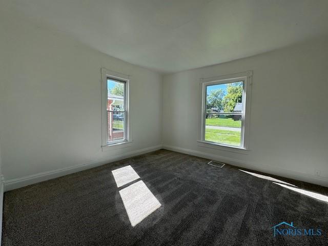 spare room featuring dark colored carpet and a wealth of natural light