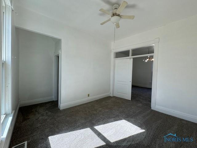 unfurnished bedroom featuring ceiling fan with notable chandelier, dark carpet, and a closet