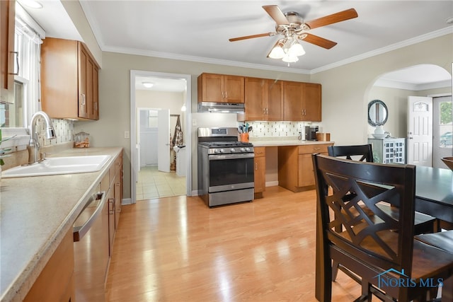 kitchen with backsplash, sink, ceiling fan, ornamental molding, and stainless steel appliances