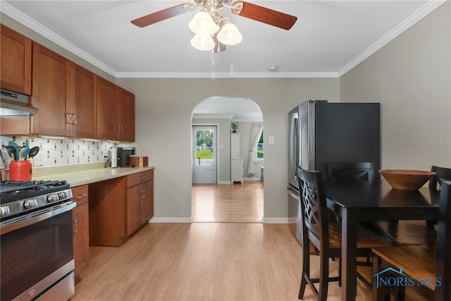 kitchen with appliances with stainless steel finishes, light wood-type flooring, backsplash, ornamental molding, and extractor fan