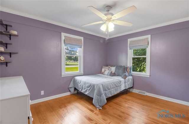 bedroom featuring ceiling fan, light wood-type flooring, ornamental molding, and multiple windows