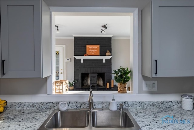 kitchen featuring a brick fireplace, light stone counters, sink, and ornamental molding