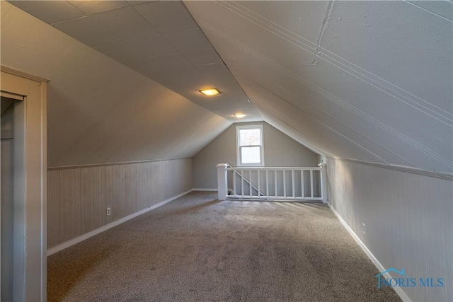 bonus room with carpet, wood walls, and vaulted ceiling