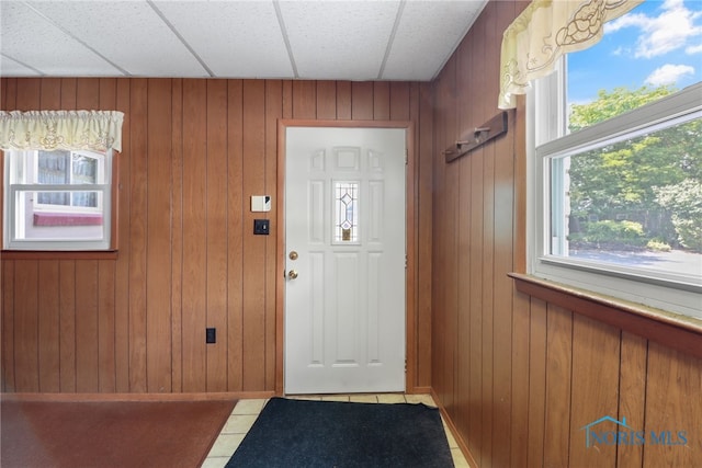 entryway featuring tile patterned floors, wood walls, and a drop ceiling