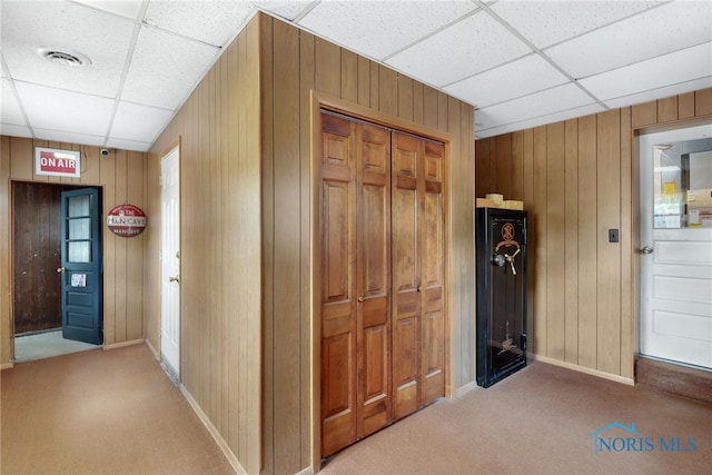 hall featuring light carpet, a drop ceiling, and wooden walls