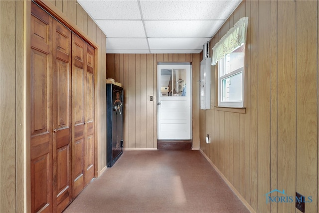 hall featuring carpet flooring, a drop ceiling, and wood walls