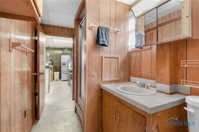 bathroom with vanity, a drop ceiling, toilet, and wooden walls