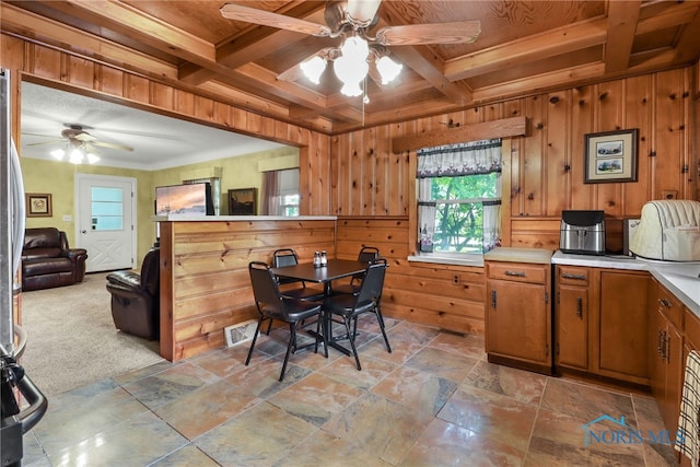 kitchen with wood walls, wooden ceiling, coffered ceiling, ceiling fan, and light colored carpet