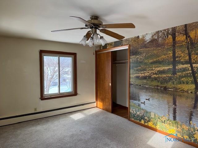 unfurnished bedroom with carpet, a closet, baseboard heating, and ceiling fan