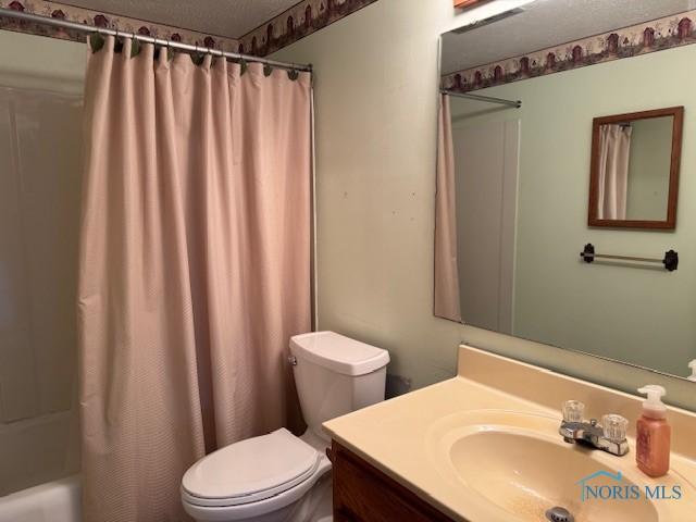 full bathroom featuring shower / bath combo with shower curtain, vanity, a textured ceiling, and toilet