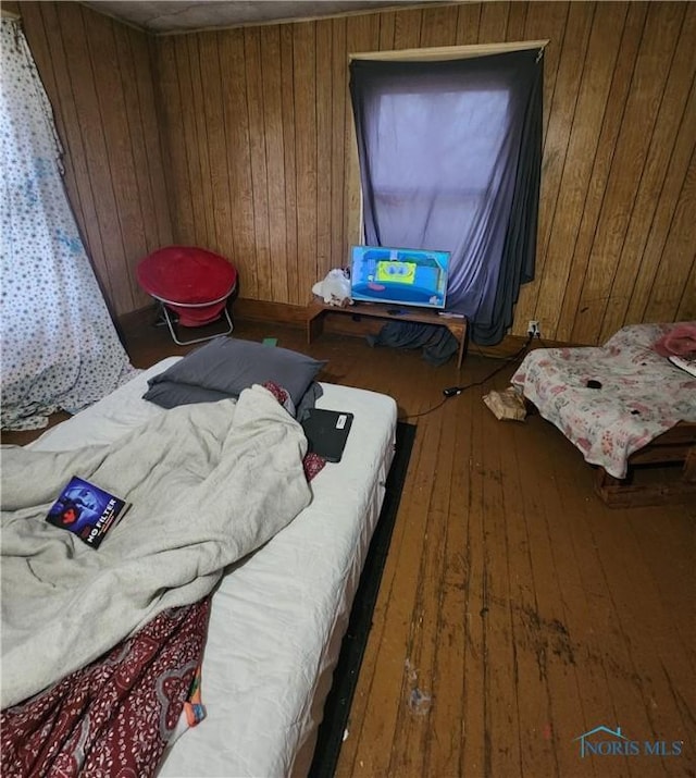 bedroom with hardwood / wood-style floors and wooden walls