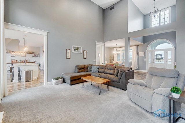 living room featuring a towering ceiling, a chandelier, and light colored carpet