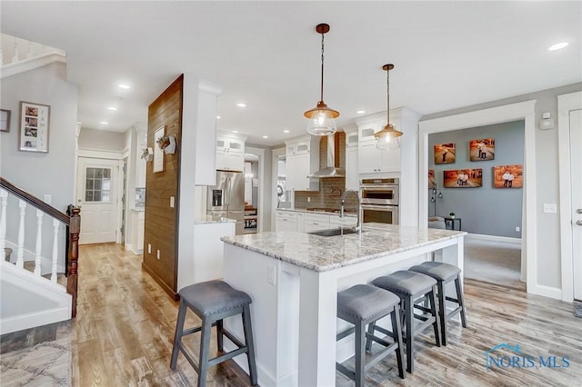 kitchen featuring light stone countertops, a breakfast bar, wall chimney range hood, white cabinets, and hanging light fixtures