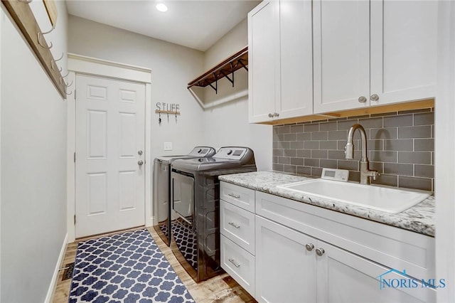 laundry room featuring washer and clothes dryer, cabinets, sink, and light hardwood / wood-style floors