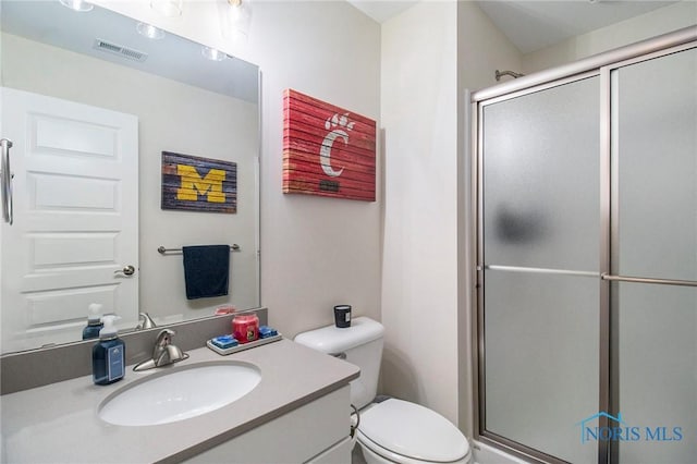 bathroom featuring a shower with door, vanity, and toilet