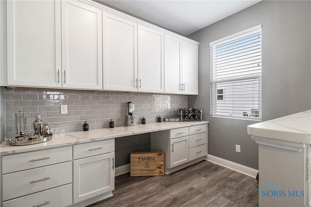 kitchen with dark wood-type flooring, light stone countertops, decorative backsplash, and white cabinets