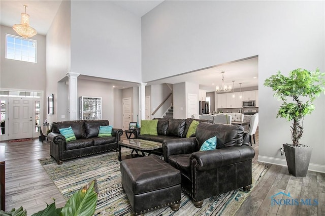 living room featuring an inviting chandelier, decorative columns, and light wood-type flooring