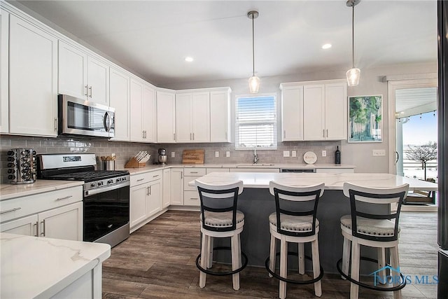 kitchen with appliances with stainless steel finishes, sink, white cabinets, and decorative light fixtures