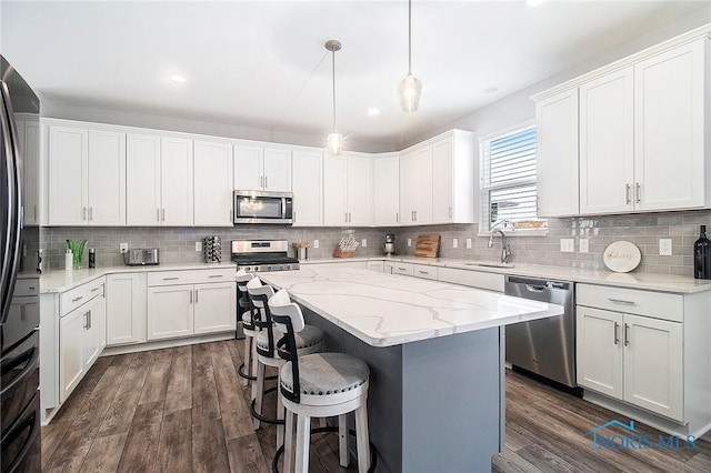 kitchen with white cabinetry, stainless steel appliances, decorative light fixtures, and a kitchen island