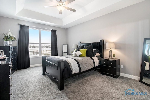 carpeted bedroom featuring a tray ceiling and ceiling fan