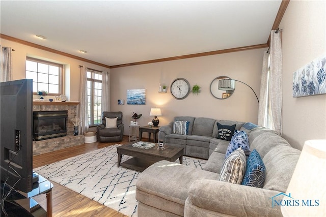 living room featuring a stone fireplace, ornamental molding, and light hardwood / wood-style flooring