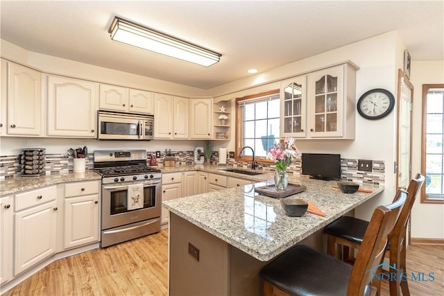 kitchen featuring kitchen peninsula, light stone counters, sink, and stainless steel appliances