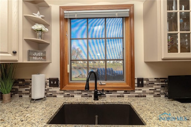 kitchen with decorative backsplash, light stone counters, and sink