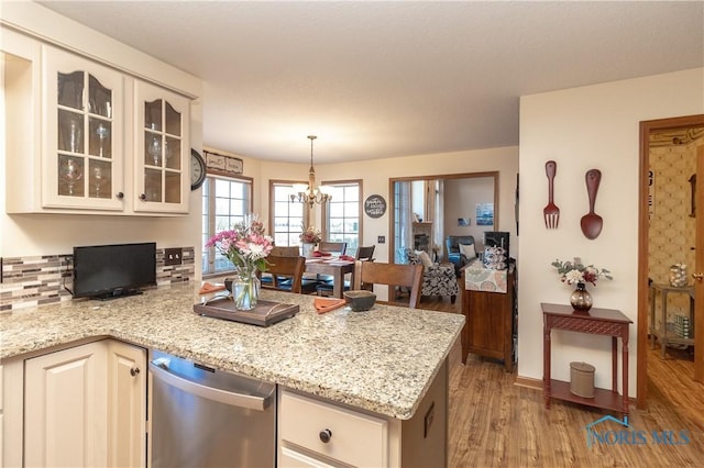 kitchen with pendant lighting, stainless steel dishwasher, decorative backsplash, a notable chandelier, and light stone counters