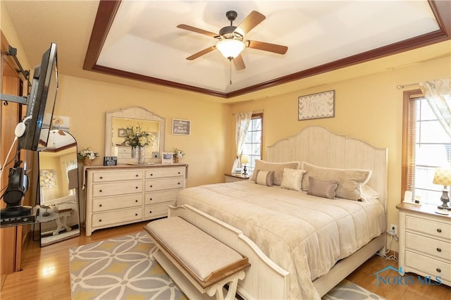 bedroom featuring hardwood / wood-style floors, a raised ceiling, ceiling fan, and crown molding