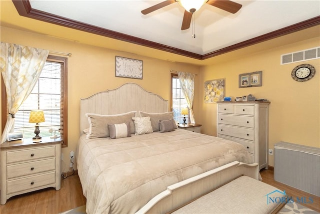 bedroom with a raised ceiling, ceiling fan, ornamental molding, and light wood-type flooring