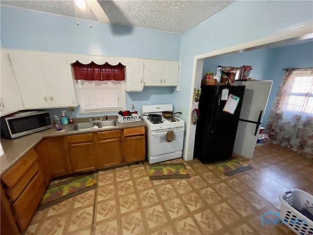 kitchen featuring white gas range oven, black fridge, a textured ceiling, sink, and white cabinets