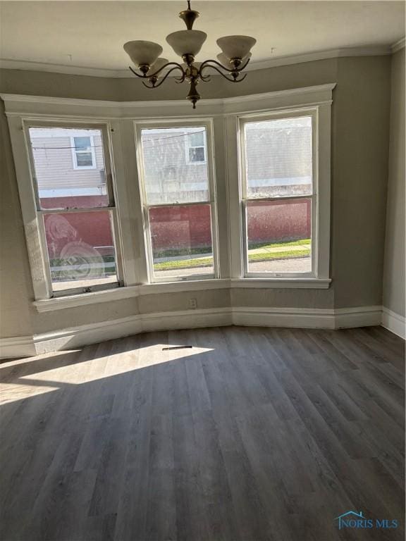 unfurnished dining area with wood-type flooring, an inviting chandelier, a wealth of natural light, and ornamental molding