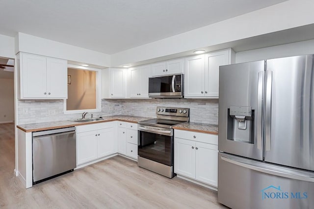 kitchen featuring appliances with stainless steel finishes, backsplash, sink, white cabinets, and light hardwood / wood-style floors