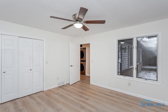 unfurnished bedroom featuring ceiling fan, light hardwood / wood-style flooring, stacked washer and dryer, and a closet