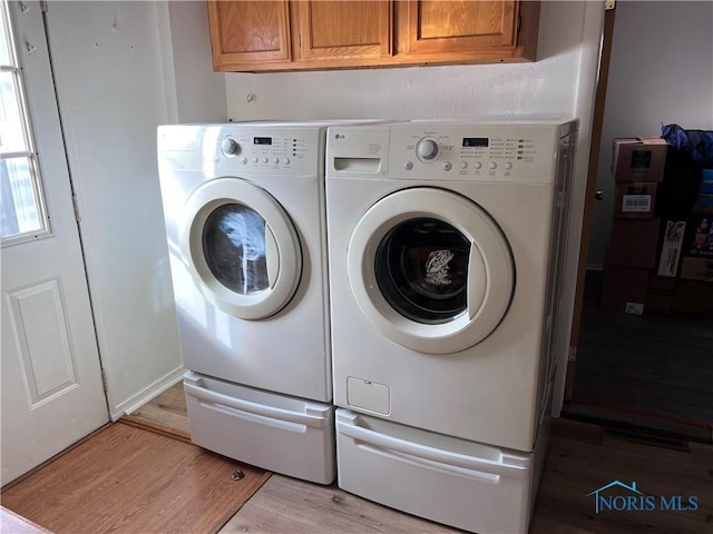 washroom with cabinets, washing machine and dryer, and light hardwood / wood-style flooring