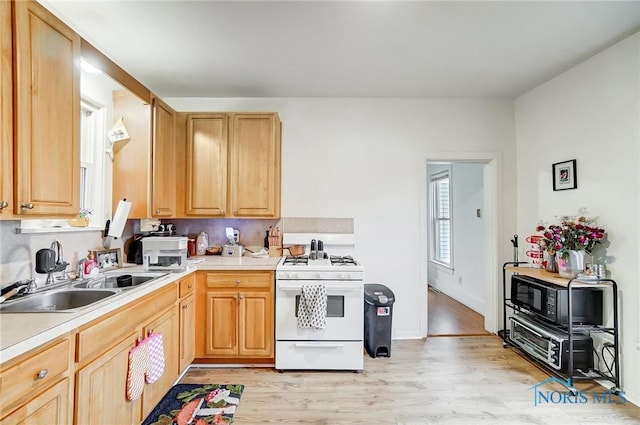 kitchen with light hardwood / wood-style floors, light brown cabinetry, sink, and white range with gas cooktop