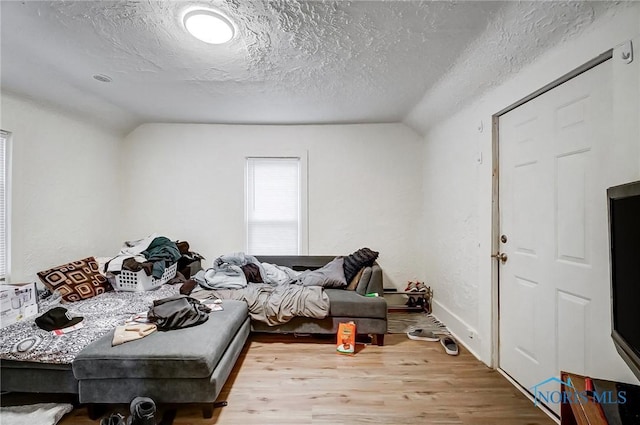 interior space featuring light wood-type flooring, a textured ceiling, and vaulted ceiling