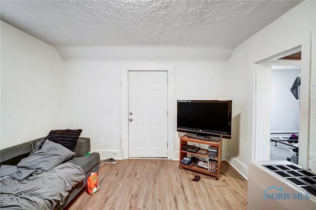 living room featuring light hardwood / wood-style flooring, baseboard heating, a textured ceiling, and vaulted ceiling