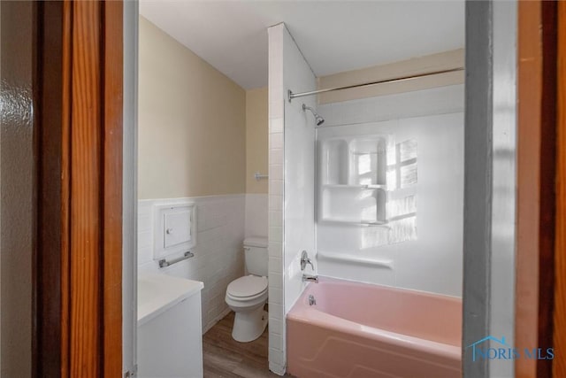 bathroom featuring  shower combination, hardwood / wood-style floors, tile walls, and toilet