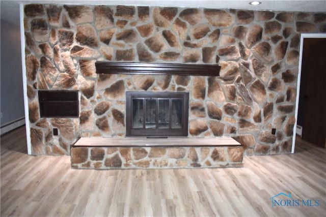 interior details featuring hardwood / wood-style flooring, a stone fireplace, and a baseboard radiator