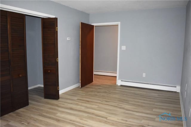 unfurnished bedroom with baseboard heating, a closet, and light hardwood / wood-style floors