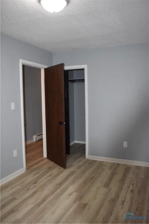 unfurnished bedroom featuring light hardwood / wood-style floors, a textured ceiling, a closet, and a baseboard radiator