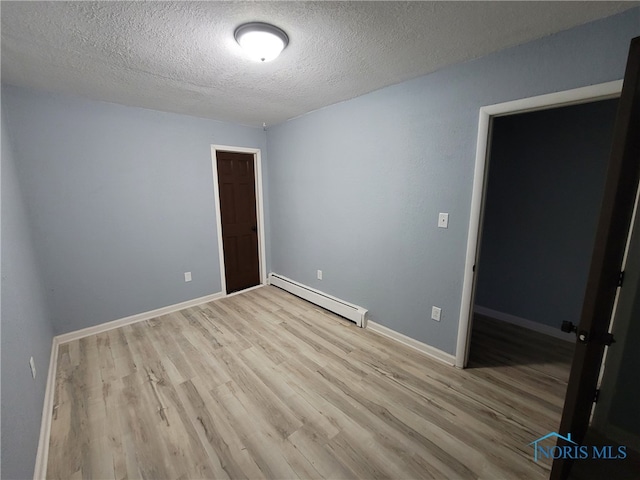 empty room with light hardwood / wood-style flooring, a textured ceiling, and a baseboard heating unit