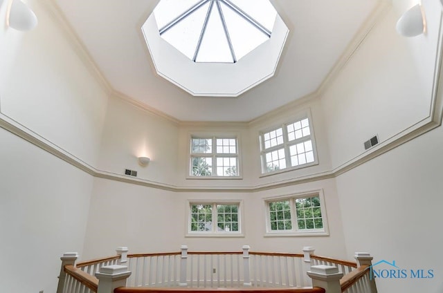 stairway with a towering ceiling, plenty of natural light, and crown molding