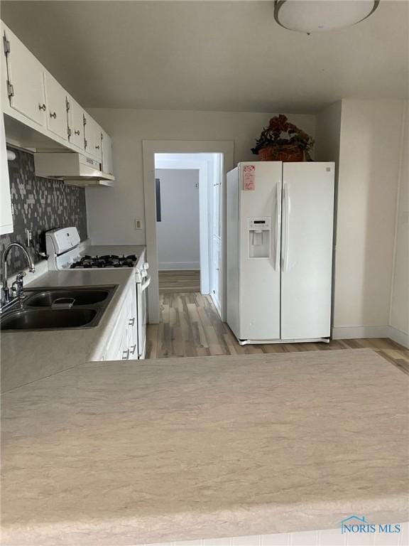 kitchen with white appliances, backsplash, white cabinets, sink, and light hardwood / wood-style flooring