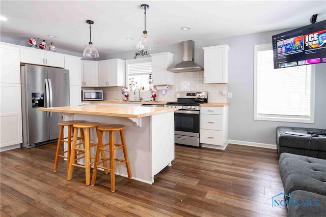 kitchen featuring backsplash, dark wood finished floors, appliances with stainless steel finishes, butcher block counters, and wall chimney range hood